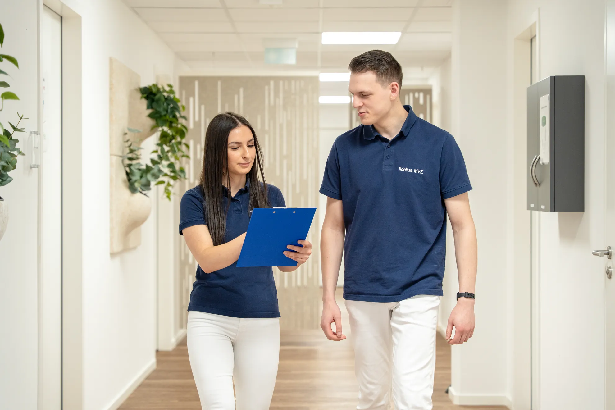 2 Personen laufen den Flur entlang und schauen ein Dokument an